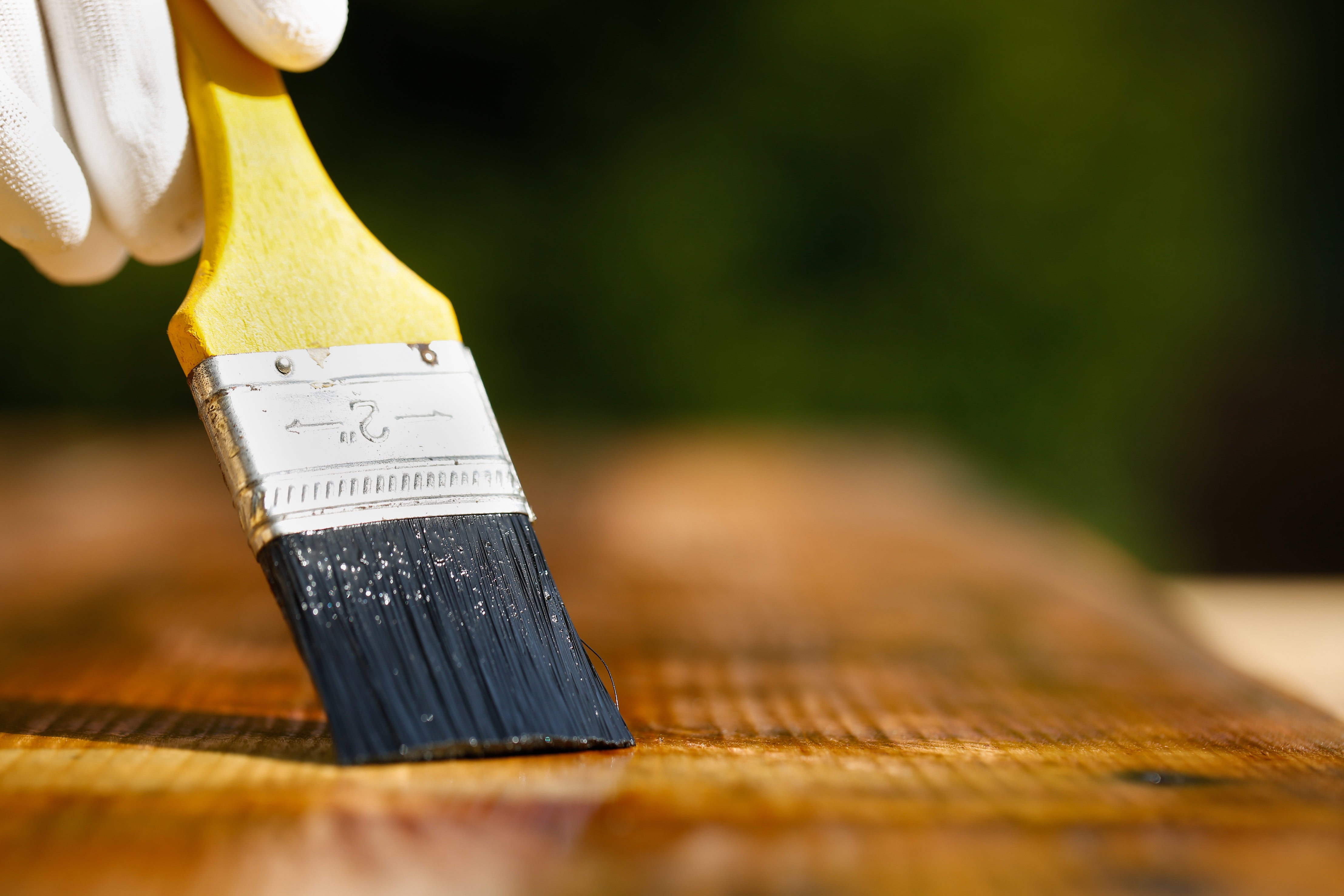 Glove covered hand painting a stain on a wood plank.