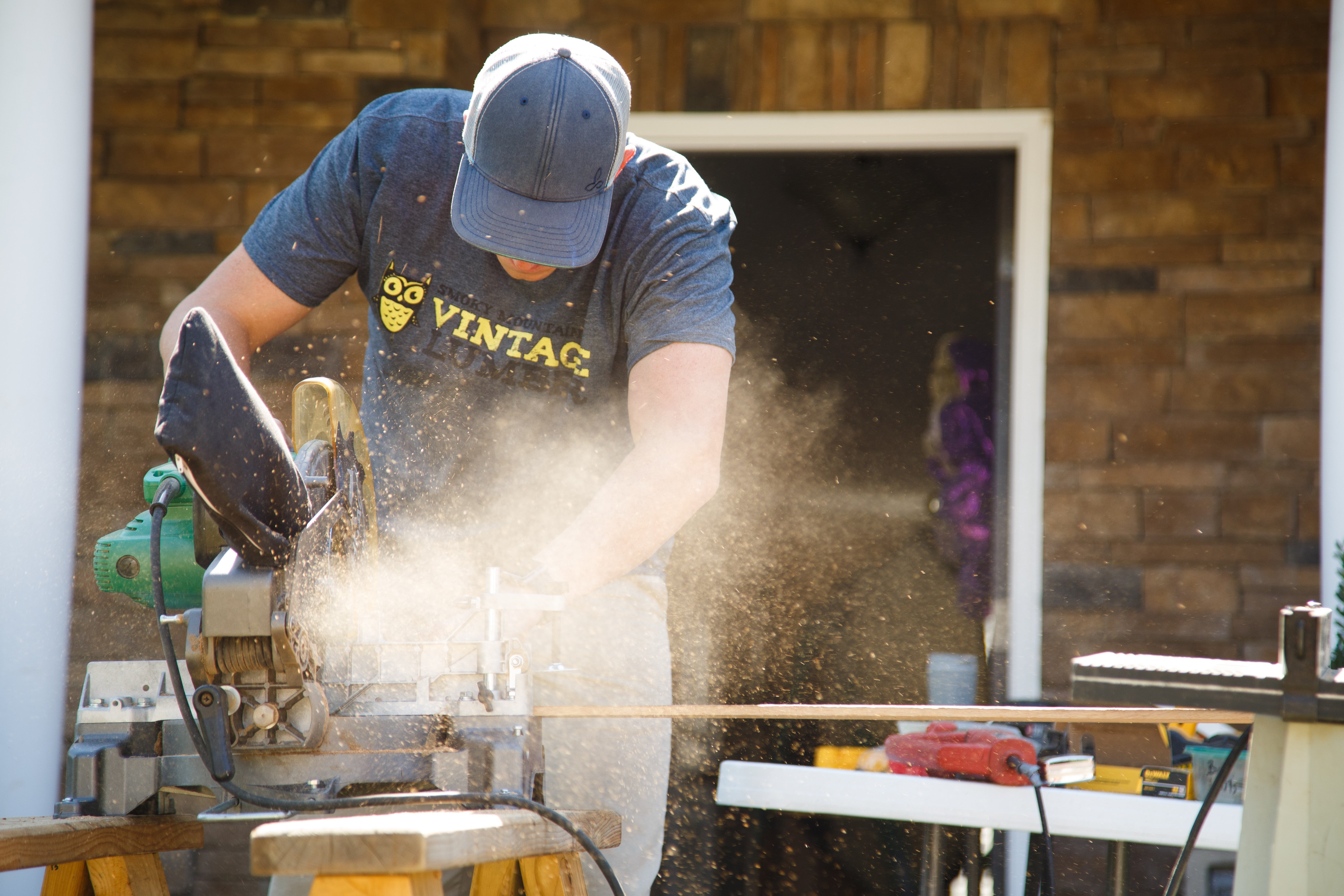 Woodworker sawing a plank outside while wearing protective gear.