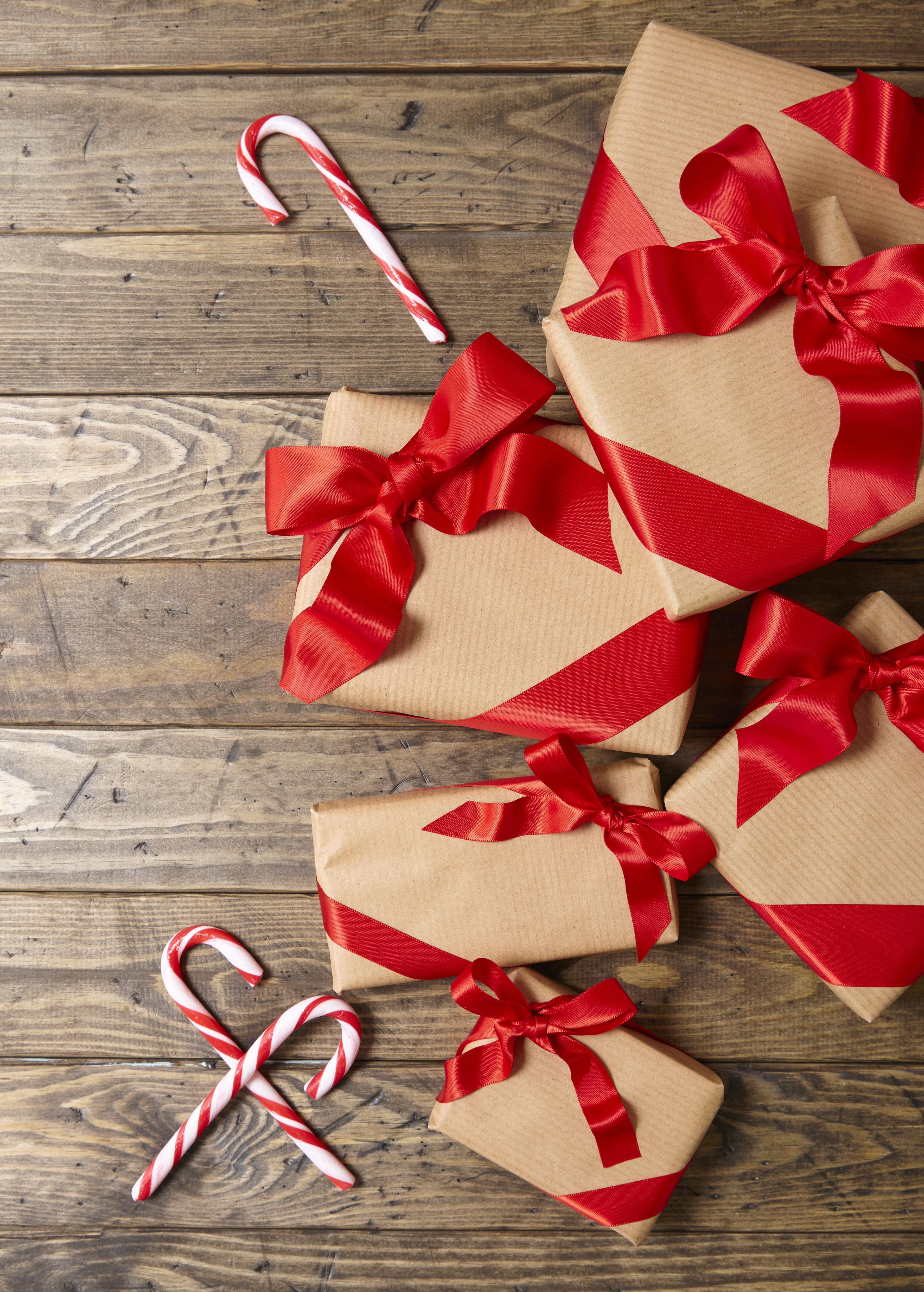 Packages wrapped in brown paper and red ribbons and candy canes on a wooden background.