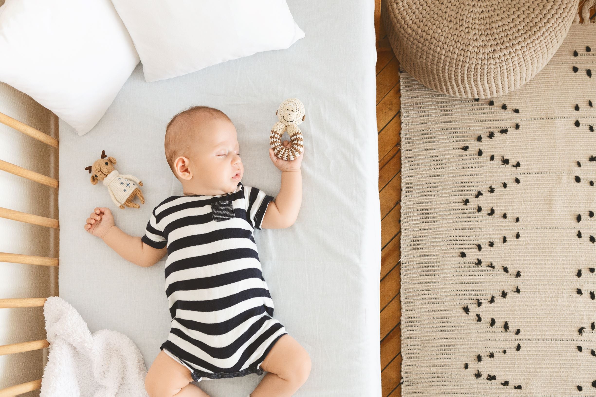 Sleeping baby in a striped onesie on a crib.