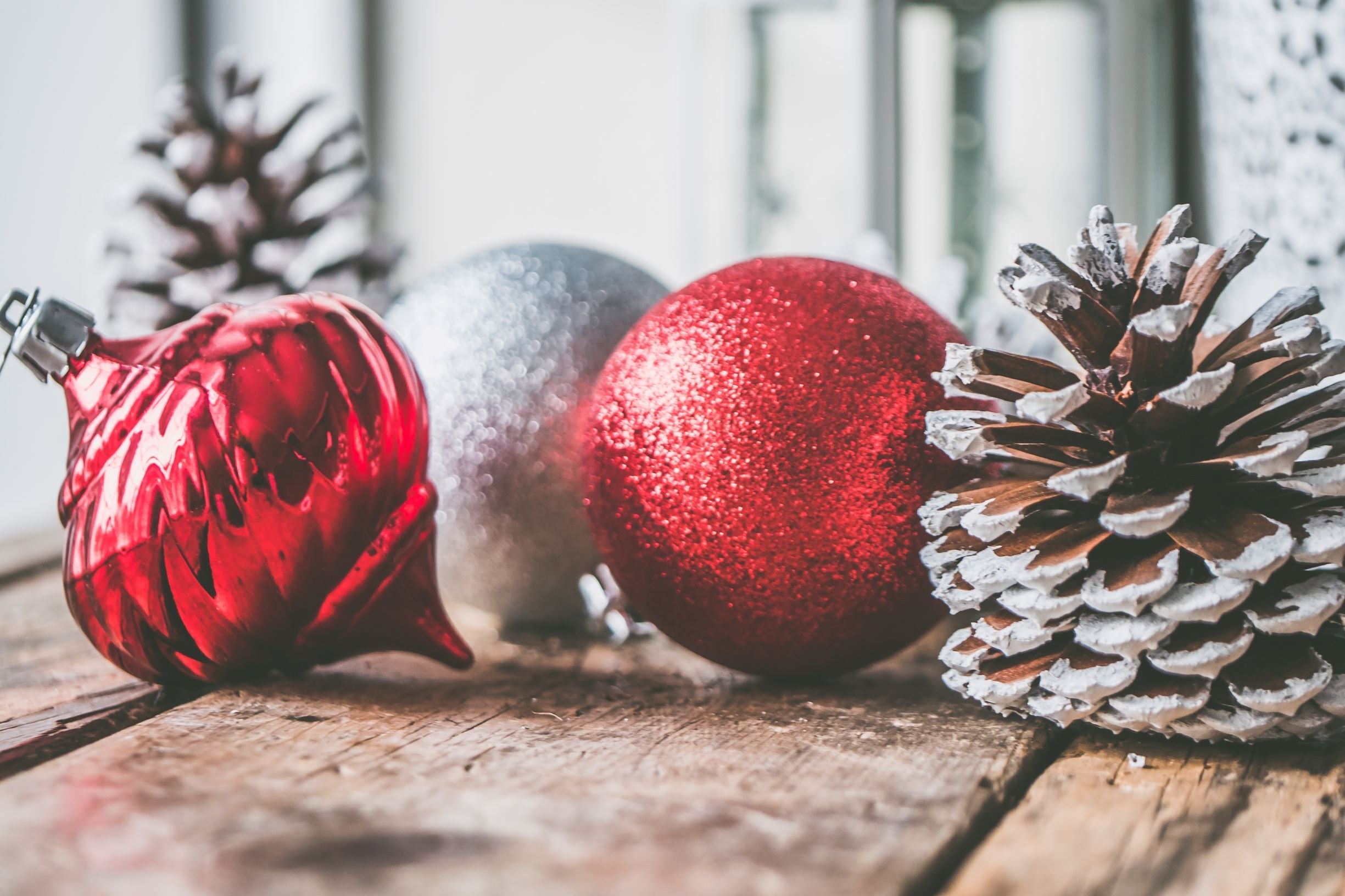Red and silver shiny Christmas tree ornaments next to a frosted pinecone.