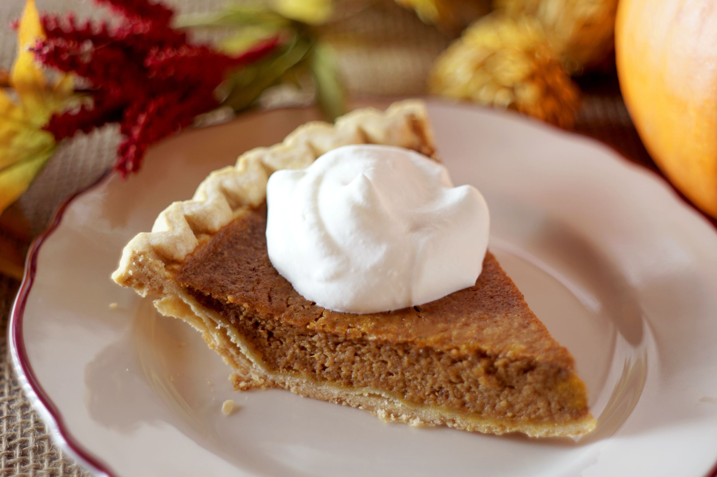 Slice of pumpkin pie and whipped cream at a Thanksgiving dinner.