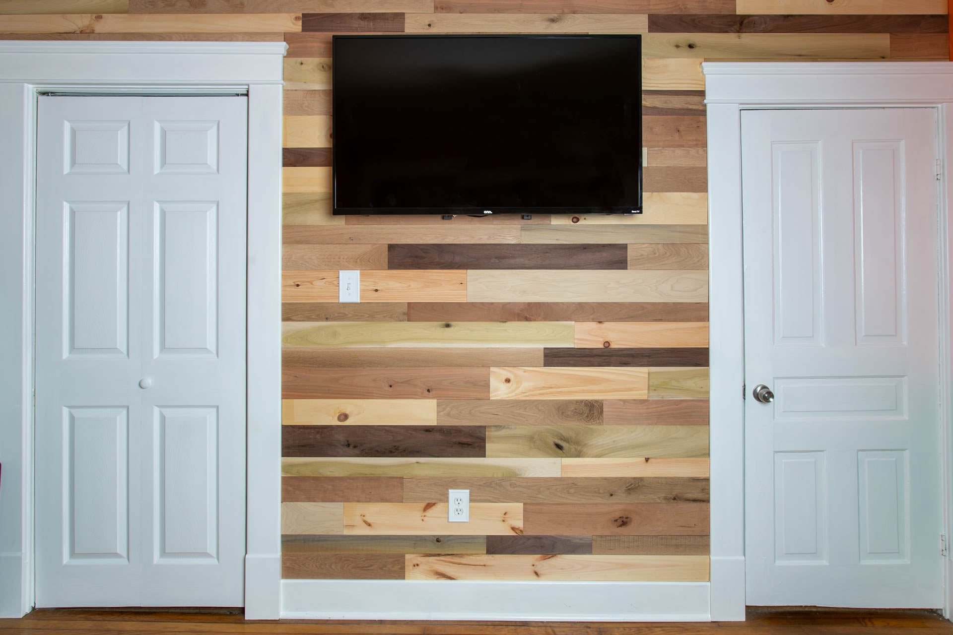 Vintage multicolored reclaimed wooden bedroom wall with a mounted TV between two closet doors.