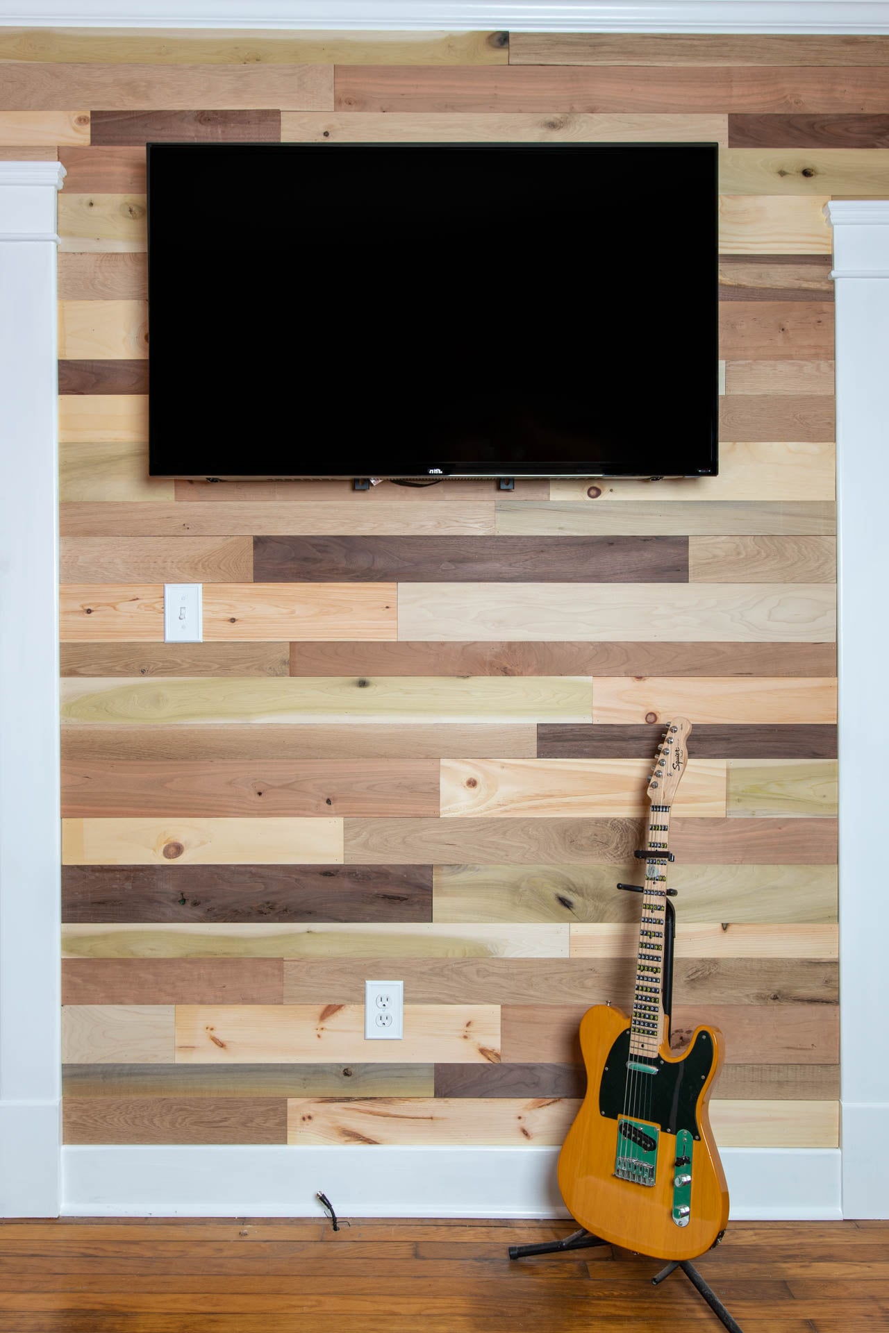 Vintage multicolored reclaimed wooden plank wall with a mounted TV and guitar.